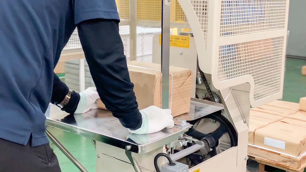 印刷会社 菱源の配送課、自動紐掛機を使っての梱包